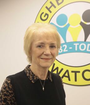Karin has blonde bobbed hair and a dark top. She is standing in front of the NW logo 