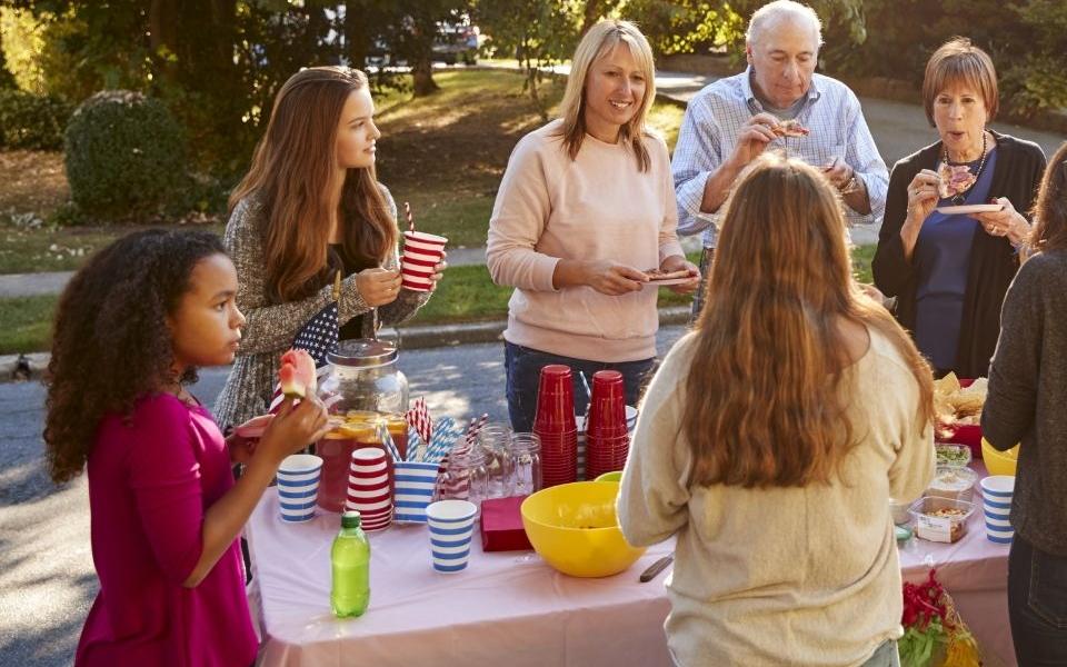 Images shows a group of neighbours eating outside. 